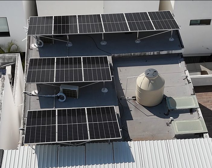 Tres filas de paneles solares elevados sobre losa, junto a minisplits y tinaco