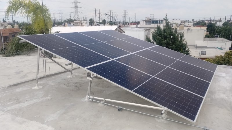 Arreglo inclinado de paneles solares sobre losa, con una palmera al fondo